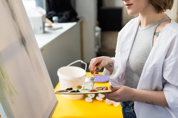 Young artistic girl holding palette and brush in light studio — Stock Photo