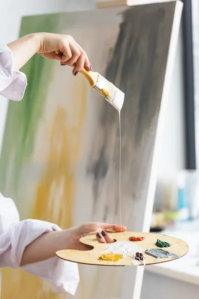 Vue rapprochée de la fille créative tenant pinceau et palette en studio lumière — Photo de stock