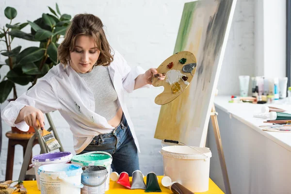 Jeune fille artistique choisissant la peinture en studio de lumière — Photo de stock