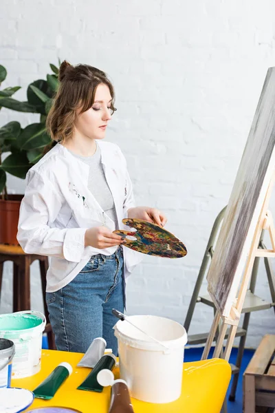 Junge künstlerische Mädchen mit Palette im hellen Atelier — Stockfoto