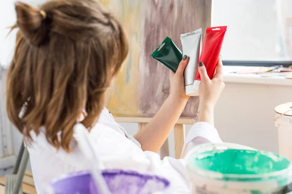 Молодая вдохновленная девушка выбирает тюбик краски в световой студии — стоковое фото