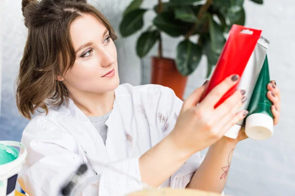 Jeune fille créative choisissant la peinture en studio de lumière — Photo de stock