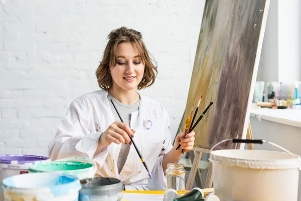 Young inspired girl with brushes in hands in light studio — Stock Photo