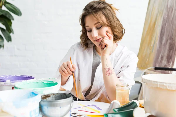 Young artistic girl painting by table in light studio — Stock Photo