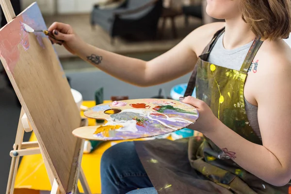 Молода дівчина надихнула дівчину застосувати ґрунтовку на полотні в світлій студії — стокове фото