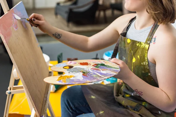 Joven chica inspirada aplicando imprimación sobre lienzo en estudio de luz - foto de stock