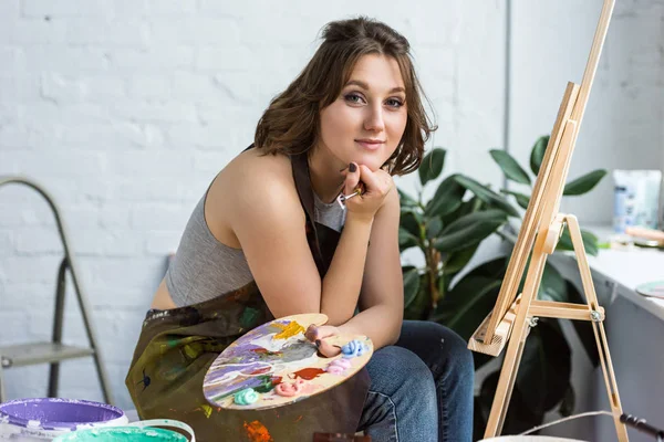 Молодая артистка с рукой на подбородке смотрит в камеру в светлой студии — стоковое фото