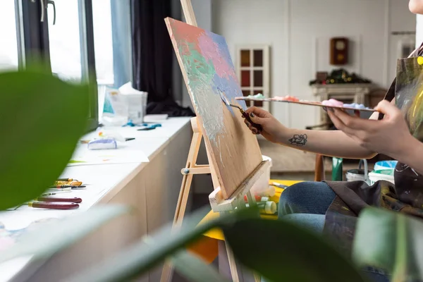 Vista de cerca de la joven chica creativa aplicando imprimación sobre lienzo en estudio de luz - foto de stock