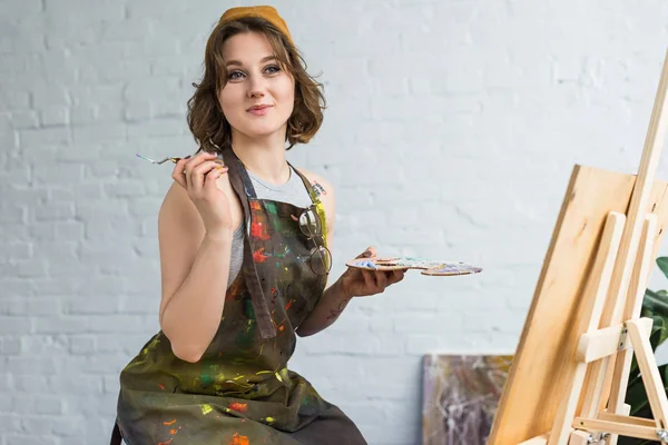 Giovane ragazza ispirata che lavora con la pittura coltello da cavalletto in studio di luce — Foto stock