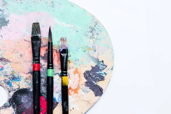 Artistic brushes on palette covered with colorful paint spots — Stock Photo