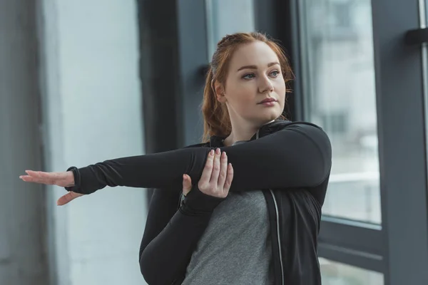Chica con sobrepeso estirando los brazos en el gimnasio - foto de stock