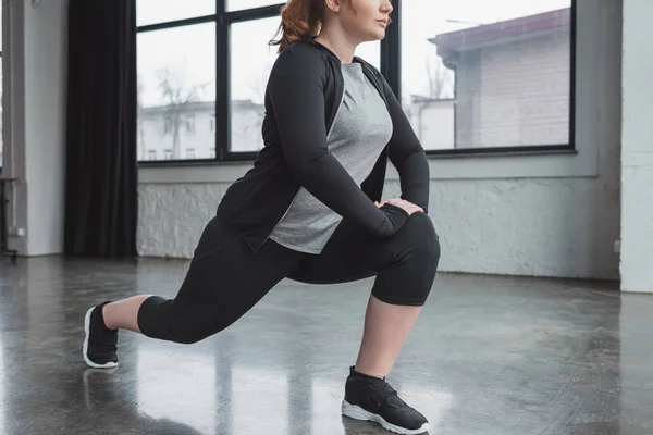 Curvy girl in gym stretching legs — Stock Photo