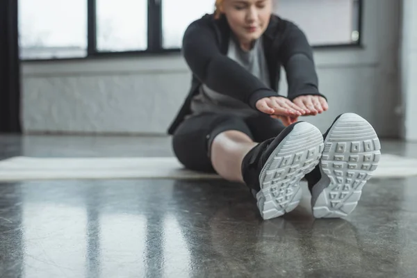 Übergewichtige Mädchen erreicht ihre Zehen in der Turnhalle — Stockfoto