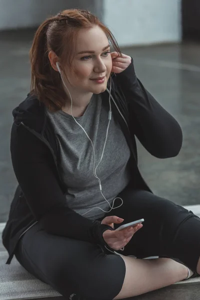 Overweight girl listening to music on smartphone in gym — Stock Photo