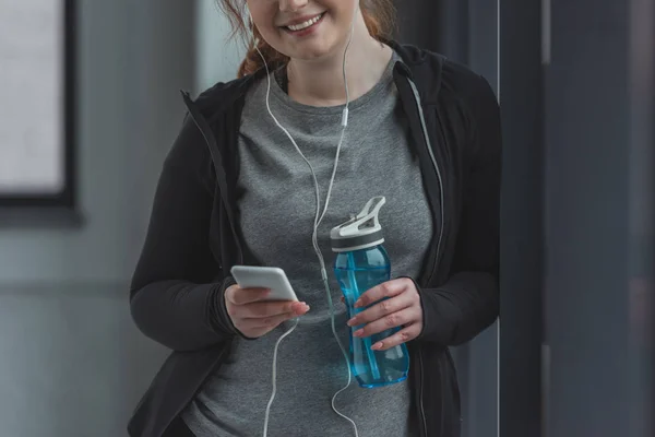 Пишна дівчина з пляшкою води слухає музику в спортзалі — стокове фото
