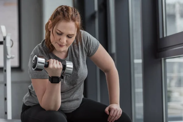 Curvy girl lifting dumbbell in gym — Stock Photo