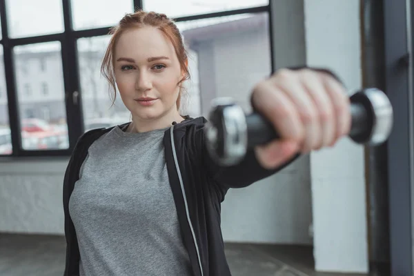 Chica con sobrepeso levantando mancuerna en el gimnasio - foto de stock