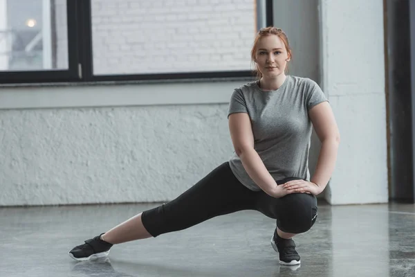 Толстая девушка растягивает ноги в спортзале — стоковое фото