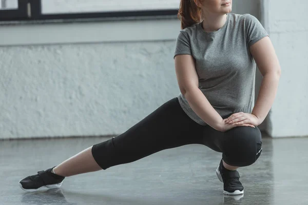 Chica con sobrepeso estirando las piernas en el gimnasio - foto de stock