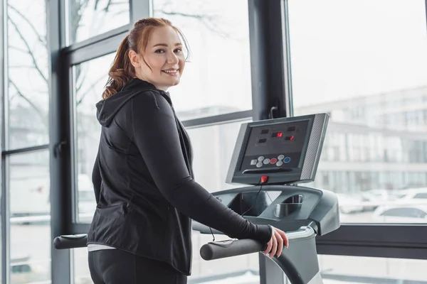 Obese girl smiling while on treadmill in gym — Stock Photo