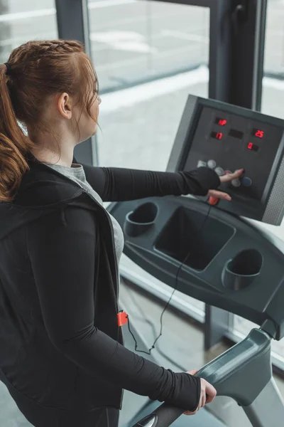 Chica curvilínea ajustando cinta de correr en el gimnasio - foto de stock