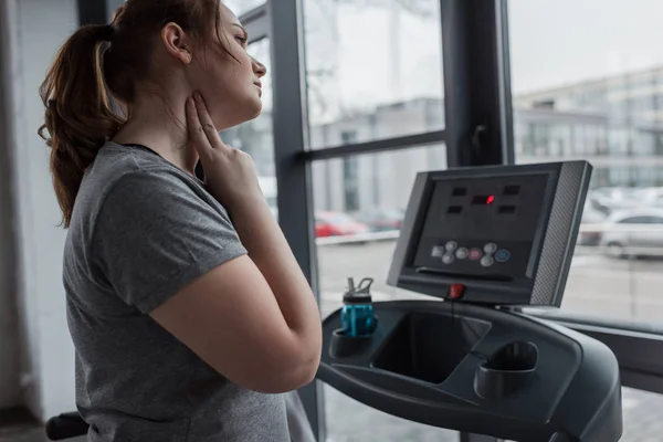 Chica con sobrepeso comprobando el pulso durante la carrera en la cinta en el gimnasio - foto de stock