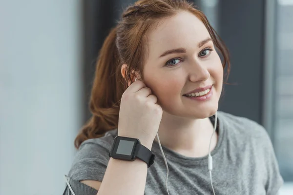 Obese girl with fitness tracker listening to music in gym — Stock Photo