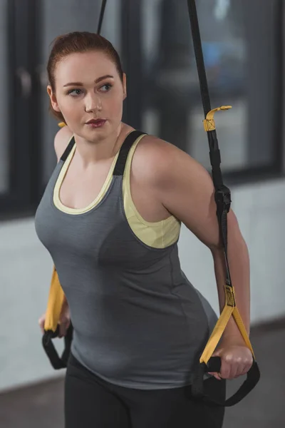 Overweight girl training on suspension straps in gym — Stock Photo