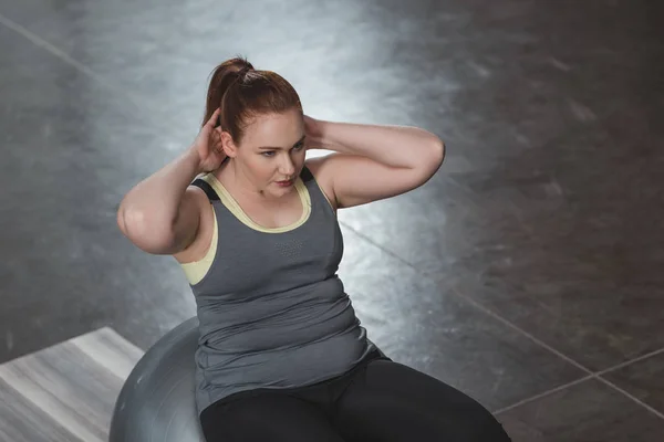 Curvy fille exerçant sur la balle de fitness dans la salle de gym — Photo de stock