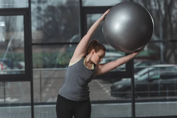 Menina curvilínea exercitando com bola de fitness no ginásio — Fotografia de Stock