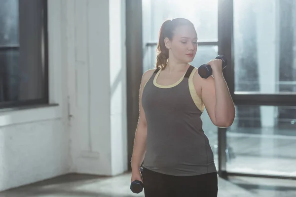 Curvy girl lifting dumbbells in gym — Stock Photo