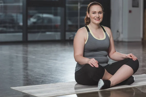 Obèse fille souriante pendant la méditation dans la salle de gym — Photo de stock