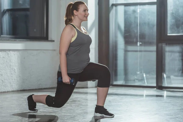 Overweight girl performing lunges with dumbbells in gym — Stock Photo