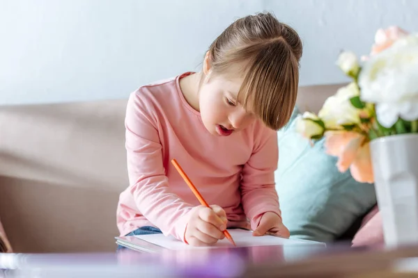 Kind mit Down-Syndrom zeichnet mit Bleistift auf Sofa — Stockfoto