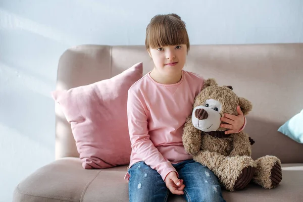 Kid with down syndrome sitting on sofa and hugging teddy bear — Stock Photo