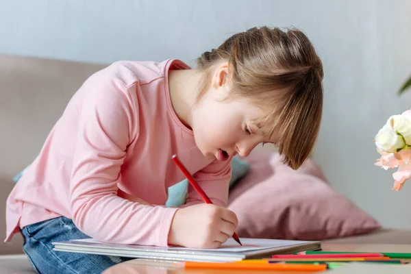 Enfant atteint du syndrome du duvet dessinant avec enthousiasme avec des crayons colorés — Photo de stock