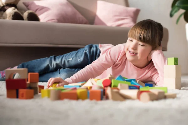 Criança com síndrome de down deitada no chão e olhando para cubos de brinquedo — Fotografia de Stock