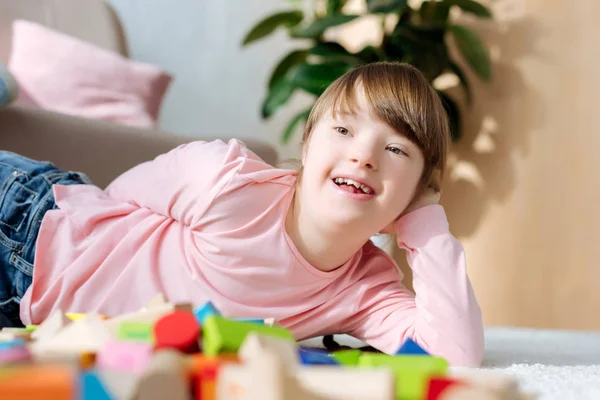 Ребенок с синдромом Дауна лежит на полу с кубиками игрушек — стоковое фото
