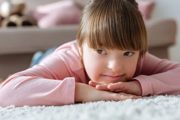 Verträumtes Kind mit Down-Syndrom liegt auf dem Boden in gemütlichem Zimmer — Stockfoto