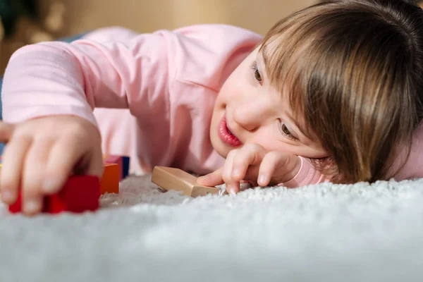 Ребенок с синдромом Дауна играет с кубиками игрушек, лежа на полу — стоковое фото