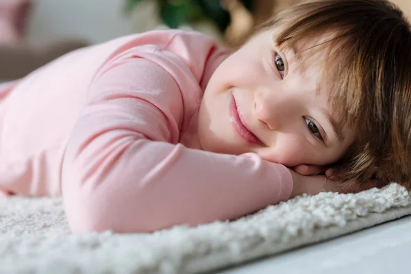 Niña sonriente con síndrome de Down acostada en una alfombra de piso suave — Stock Photo