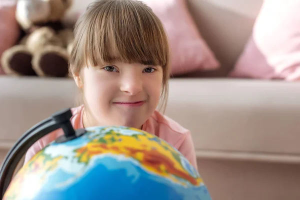 Kid with down syndrome looking at camera over globe — Stock Photo