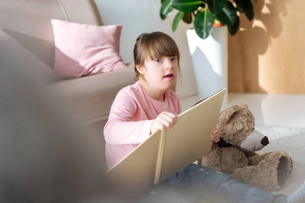 Niño con síndrome de Down libro de lectura mientras está sentado en el suelo - foto de stock