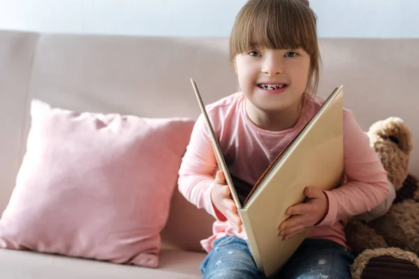 Laughing kid with down syndrome reading book — Stock Photo