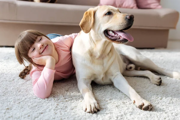 Criança feliz com síndrome de down deitada no chão com Labrador retriever — Fotografia de Stock