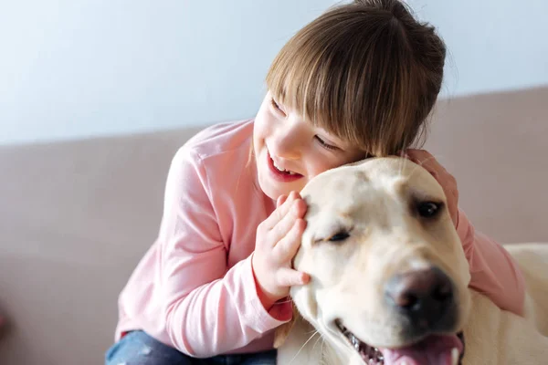 Kid with down syndrome hugging dog on sofa — Stock Photo