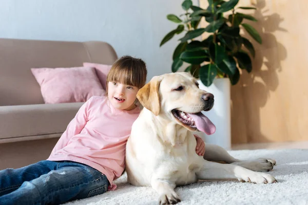 Child with down syndrome hugging Labrador retriever on the floor — Stock Photo
