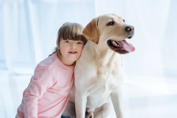 Kid girl with down syndrome embracing Labrador retriever on light background — Stock Photo