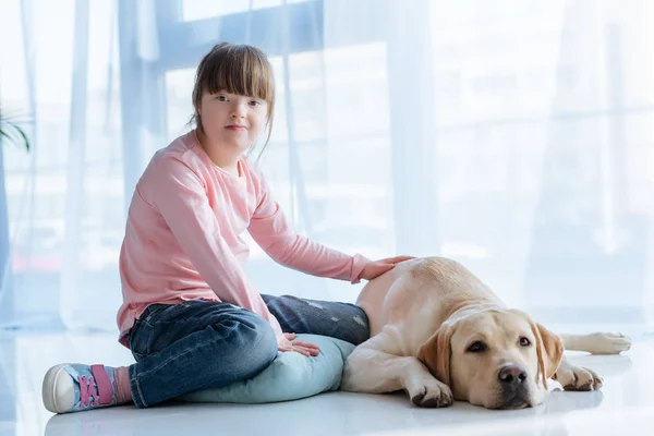 Niño con síndrome de Down sentado en el suelo con Labrador retriever - foto de stock