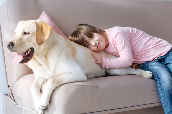 Kid with down syndrome lying on the sofa with Labrador retriever dog — Stock Photo